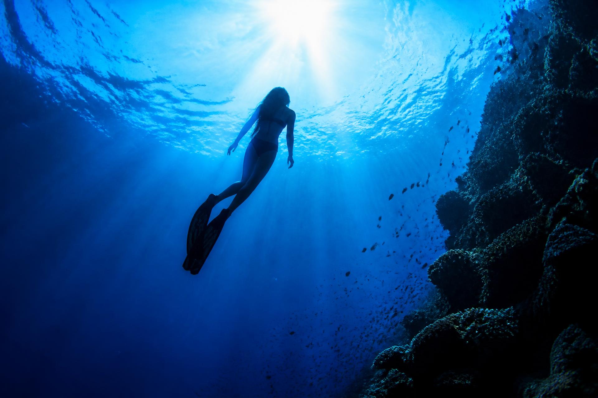 Woman freediving toward the sunlit surface of deep blue water
